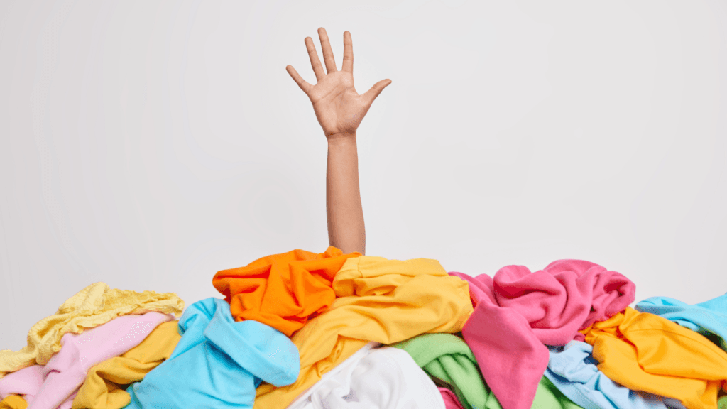 A hand reaching out of a pile of clothes begging for a closet clean out.